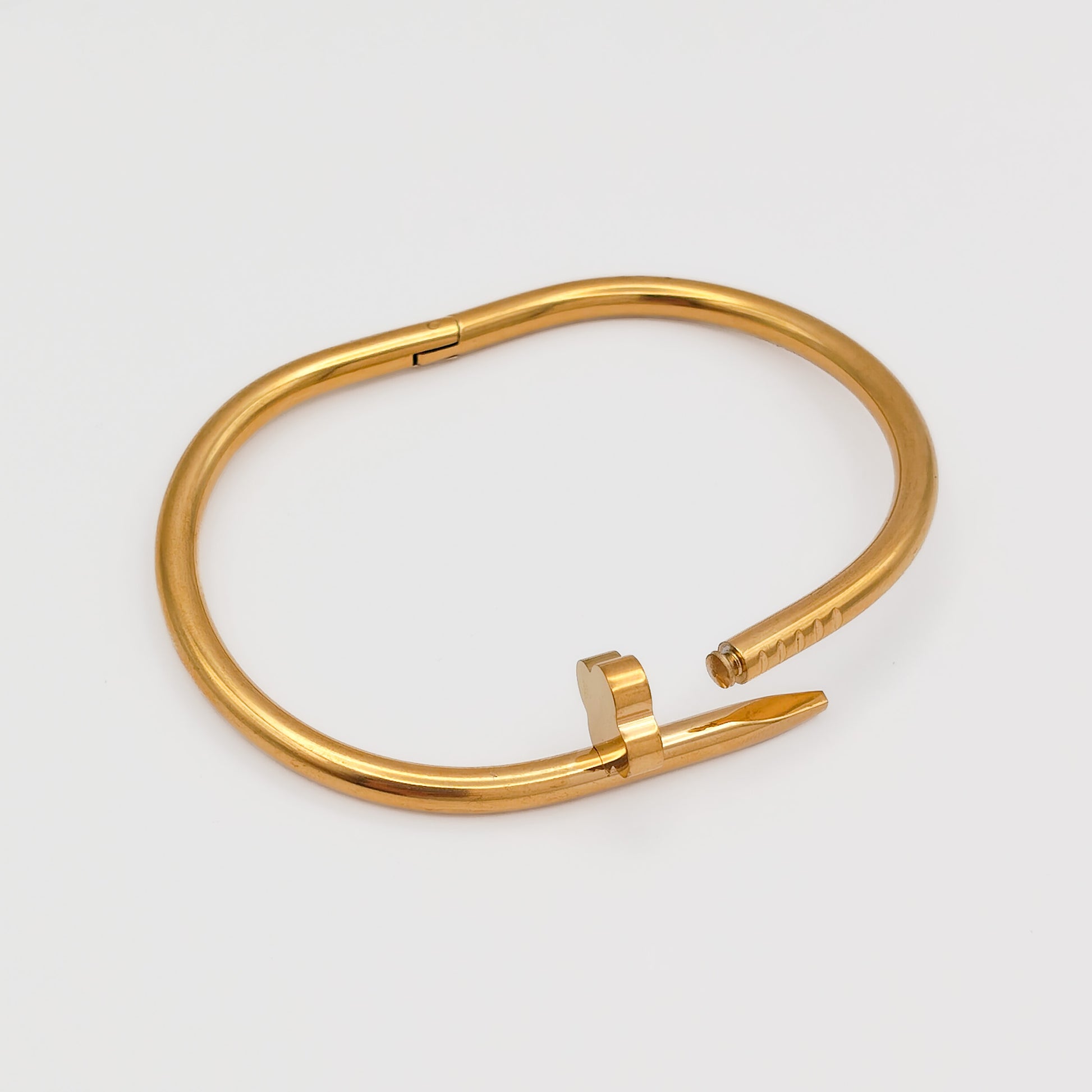 The gold plated nail bangle unclasped and open, detailing the secure internal hinge mechanism and seamless interlocking pin closure.