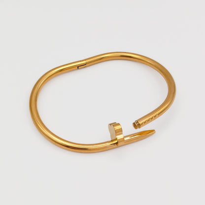 The gold plated nail bangle unclasped and open, detailing the secure internal hinge mechanism and seamless interlocking pin closure.