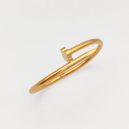 Gold-plated stainless steel nail hinge bangle shown at an angle against a white background, highlighting its sleek, reflective finish and industrial silhouette.