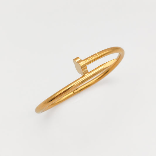 Gold-plated stainless steel nail hinge bangle shown at an angle against a white background, highlighting its sleek, reflective finish and industrial silhouette.