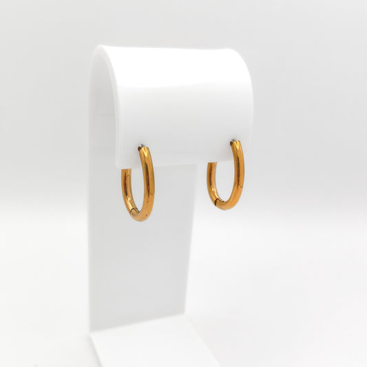 A pair of gold-plated stainless steel oval huggie hoop earrings featuring a smooth, polished surface and a seamless hinge clasp, displayed on a white stand.