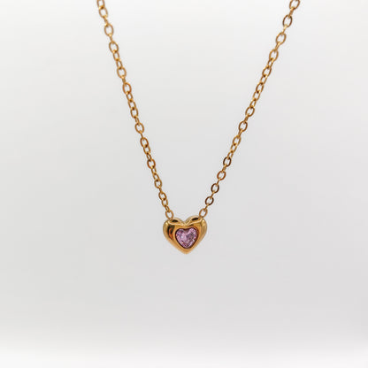Delicate gold-plated stainless steel chain necklace with a petite heart pendant featuring a sparkling pink cubic zirconia stone, showcased on a white display stand.
