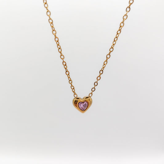 Delicate gold-plated stainless steel chain necklace with a petite heart pendant featuring a sparkling pink cubic zirconia stone, showcased on a white display stand.