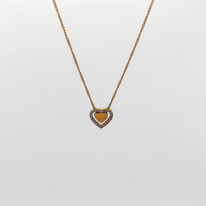 A close-up view of the gold heart-in-heart pendant, showcasing the smooth polished inner heart nestled inside a border of pavé-set clear rhinestones.