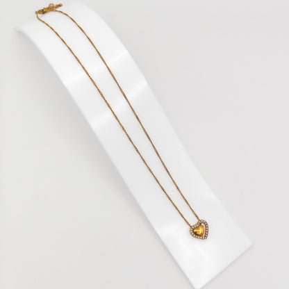 A gold-plated stainless steel princess-length chain necklace with a double heart pendant featuring a sparkling crystal rhinestone outer frame, displayed on a curved white stand.