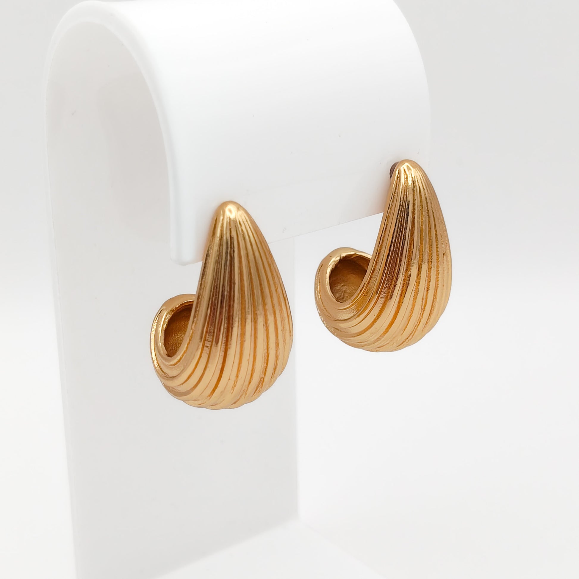 Pair of gold-plated stainless steel ribbed teardrop stud earrings displayed on a white stand, showcasing a textured, water-resistant design.