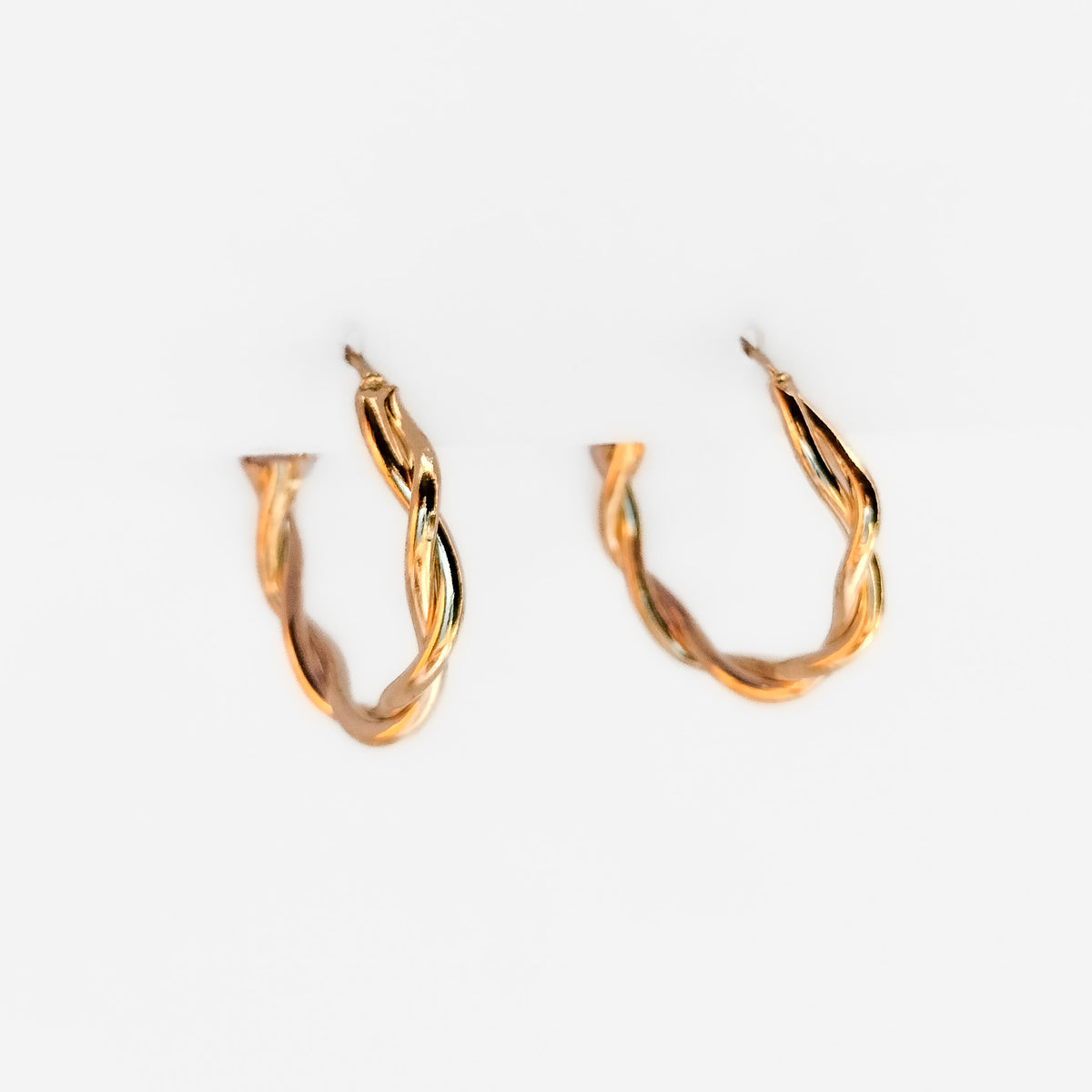 gold plated twisted hoop earrings hanging on a white display