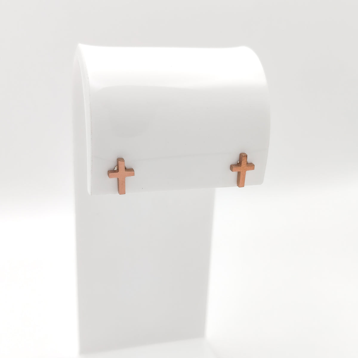 Pair of rose gold-plated cross stud earrings on a white display stand.