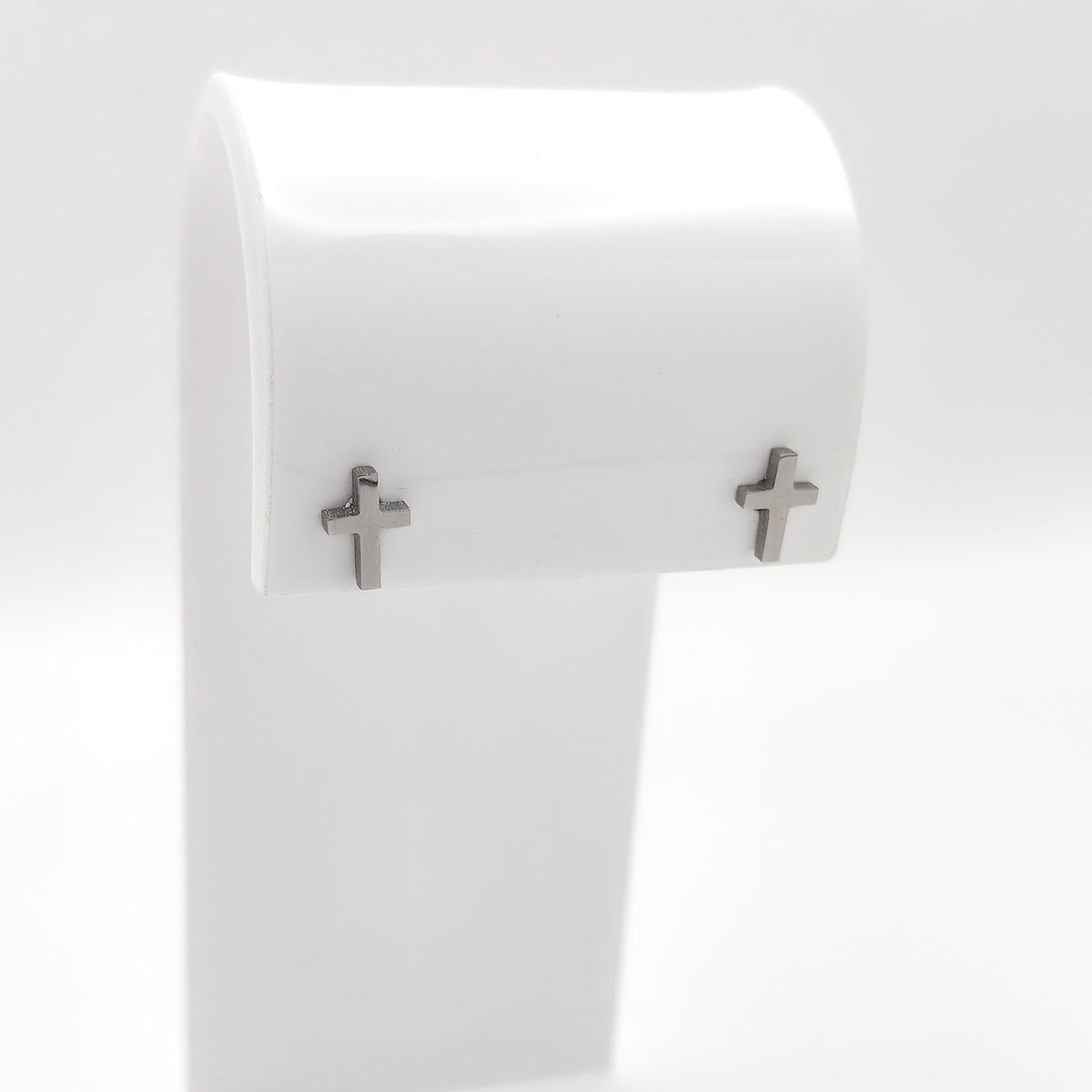 Pair of silver-plated cross stud earrings on a white display stand.