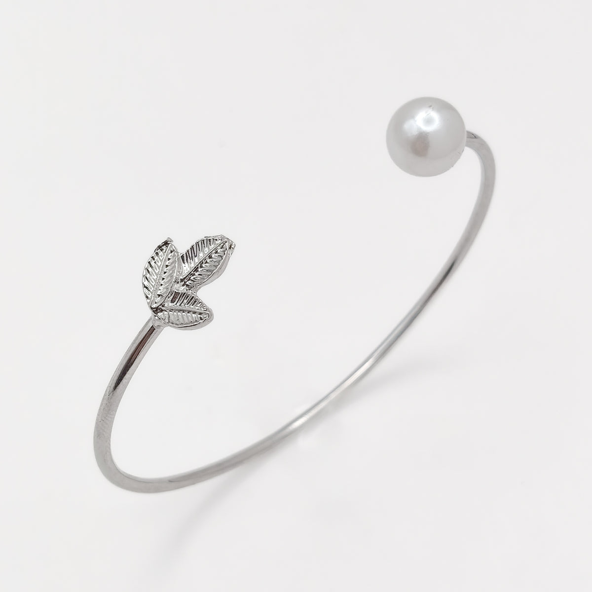 Close-up of a silver-plated cuff bangle showing textured leaves and a round white pearl-effect bead.