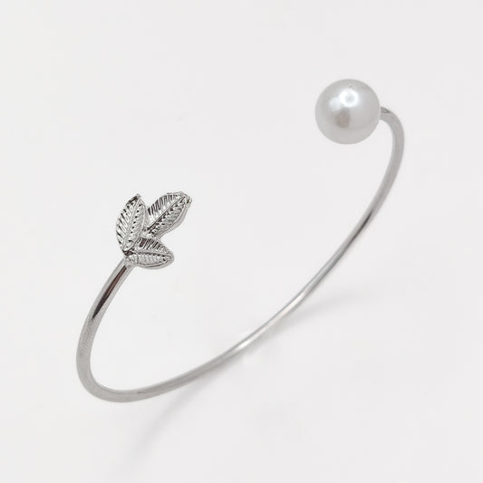 Close-up of a silver-plated cuff bangle showing textured leaves and a round white pearl-effect bead.