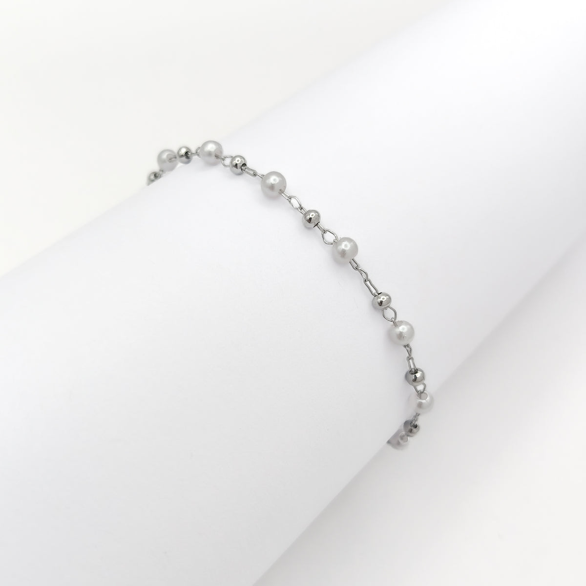 Silver-plated bracelet with white pearl beads and small silver-tone beads draped over a white display.