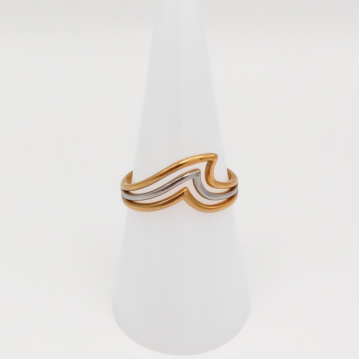 Mixed-metal adjustable stainless steel ring with a layered gold and silver wave design, displayed on a white cone stand.