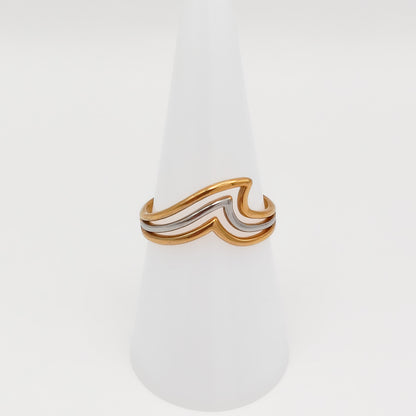 Mixed-metal adjustable stainless steel ring with a layered gold and silver wave design, displayed on a white cone stand.