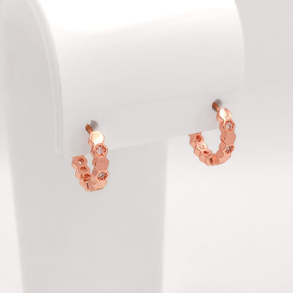 A pair of small rose gold hoop earrings with a textured honeycomb design and clear rhinestone accents, displayed on a white jewelry stand.