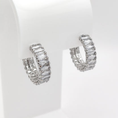 A pair of 22mm silver-toned hoop earrings set with clear rectangular baguette-cut stones, displayed on a white jewelry stand against a white background.