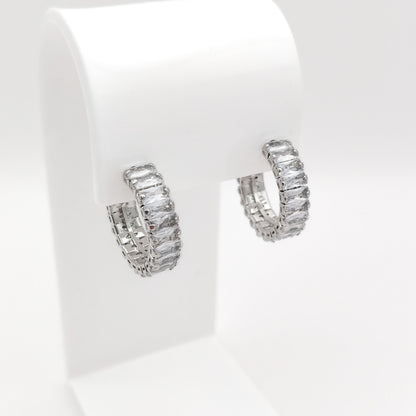 A pair of 22mm silver-plated half-hoop earrings paved with rectangular clear baguette-cut stones, displayed on a white jewelry stand against a white background.