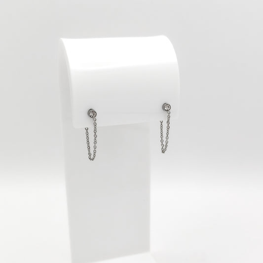 A pair of silver-toned dangle earrings with small round stud tops and short hanging chains, displayed on a white jewelry stand against a light gray background.