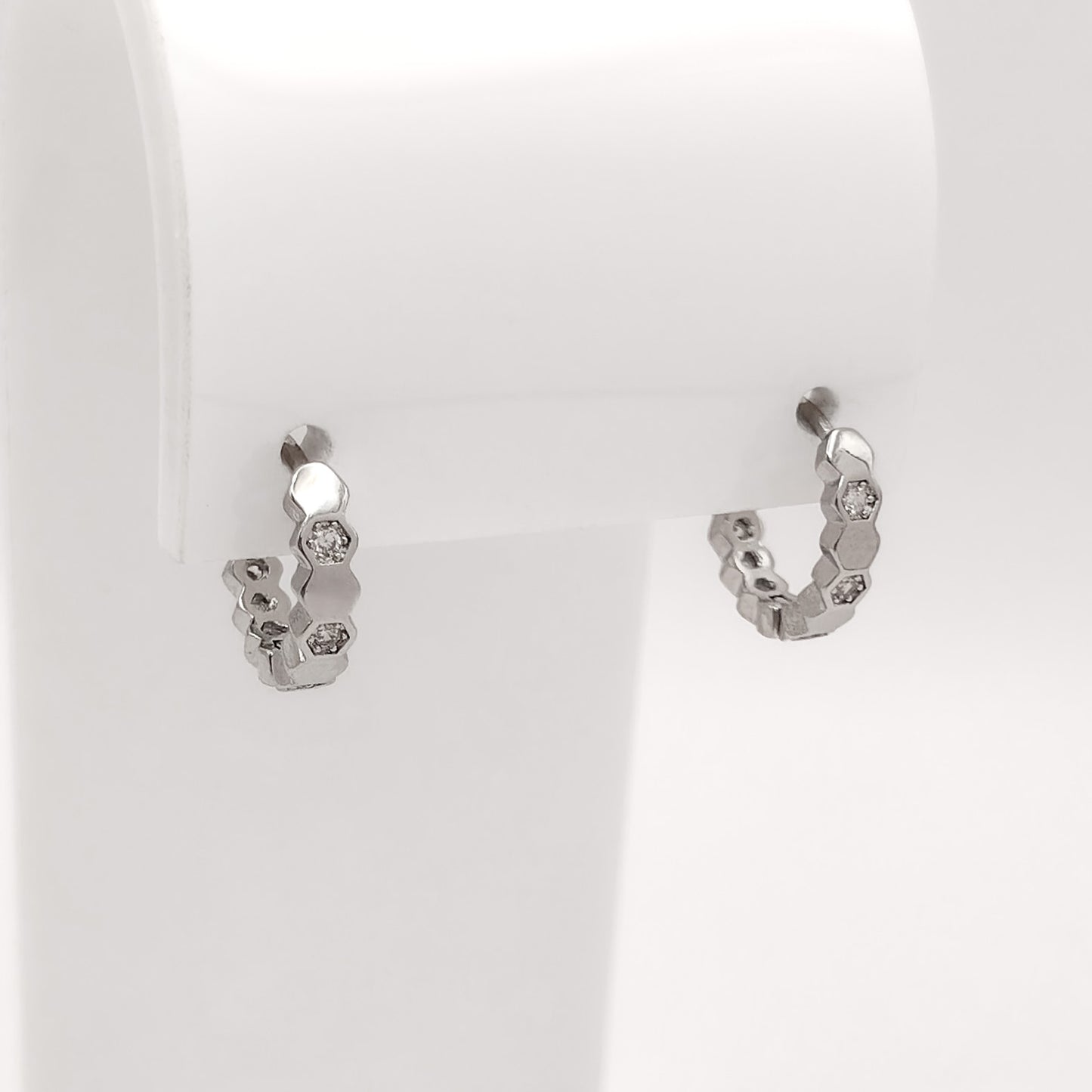 A pair of small silver hoop earrings with textured, organic shapes and clear stones, displayed on a white jewelry stand.
