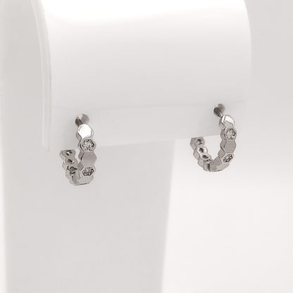 A pair of small silver hoop earrings with textured, organic shapes and clear stones, displayed on a white jewelry stand.