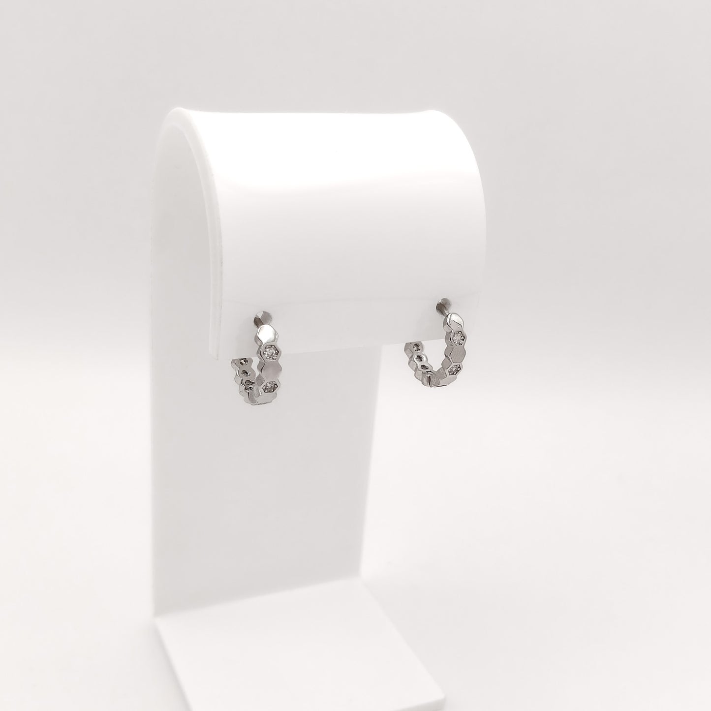 A pair of small silver hoop earrings with a textured, hammered finish, displayed on a white jewelry stand against a light gray background.