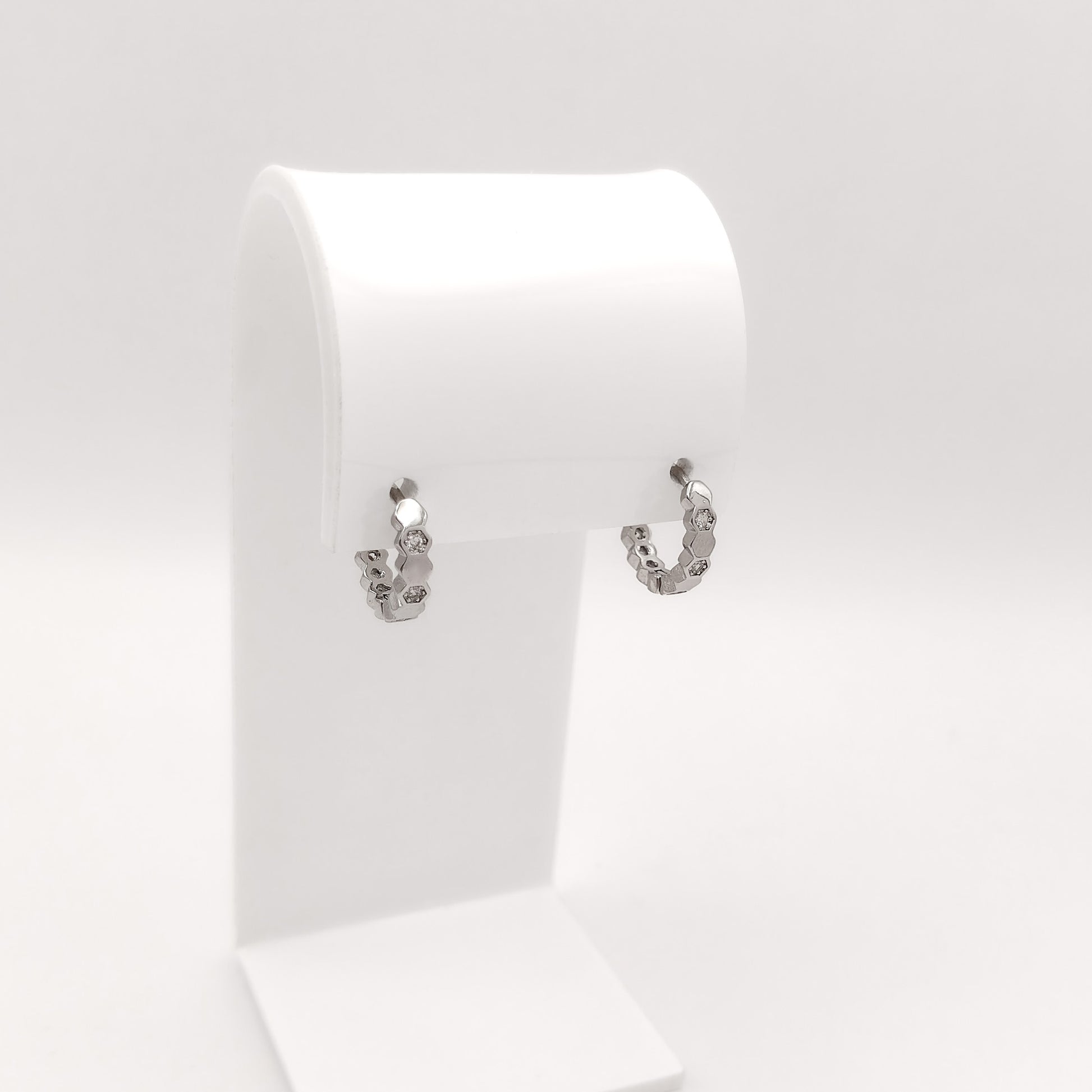 A pair of small silver hoop earrings with a textured, hammered finish, displayed on a white jewelry stand against a light gray background.