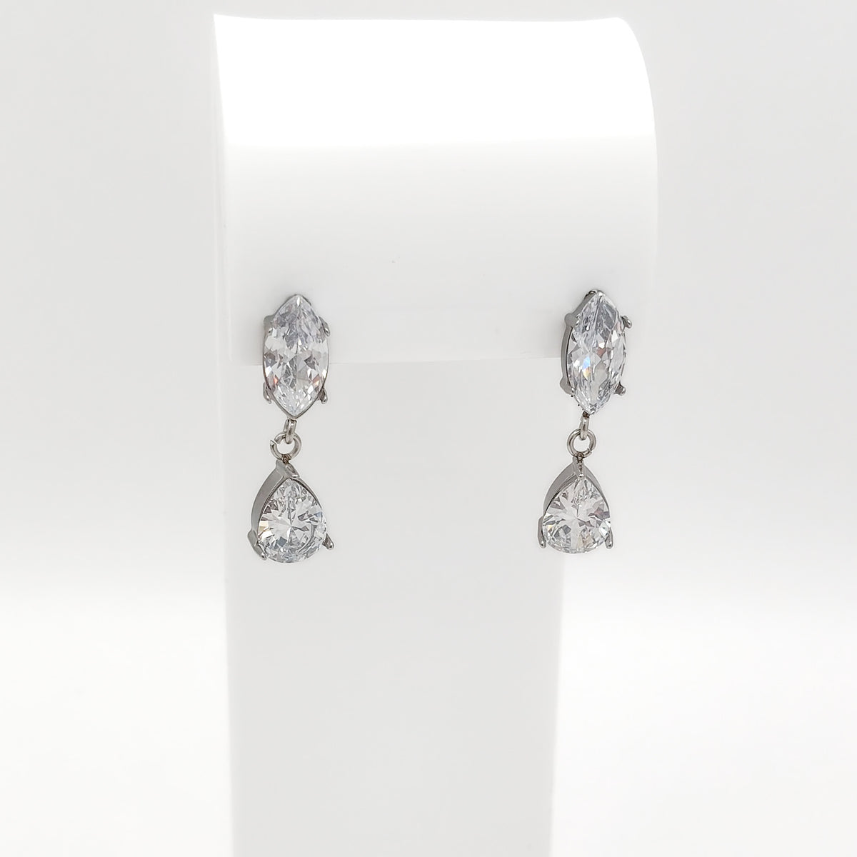 A pair of silver-tone drop earrings with marquise-cut and pear-cut clear gemstones, displayed on a white jewelry stand against a white background.