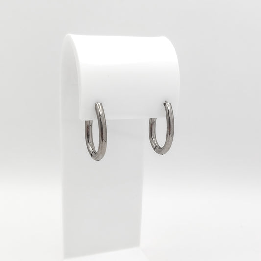 A pair of polished silver hoop earrings displayed on a white plastic jewelry stand against a clean white background.
