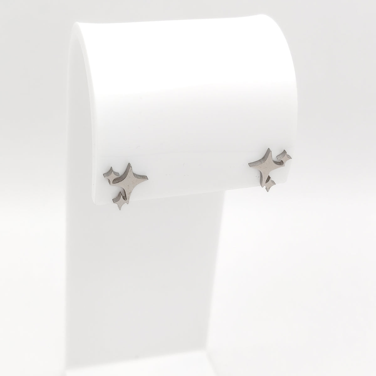 A pair of silver-plated stainless steel starburst sparkle stud earrings with a smooth polished metallic finish, displayed on a white stand.