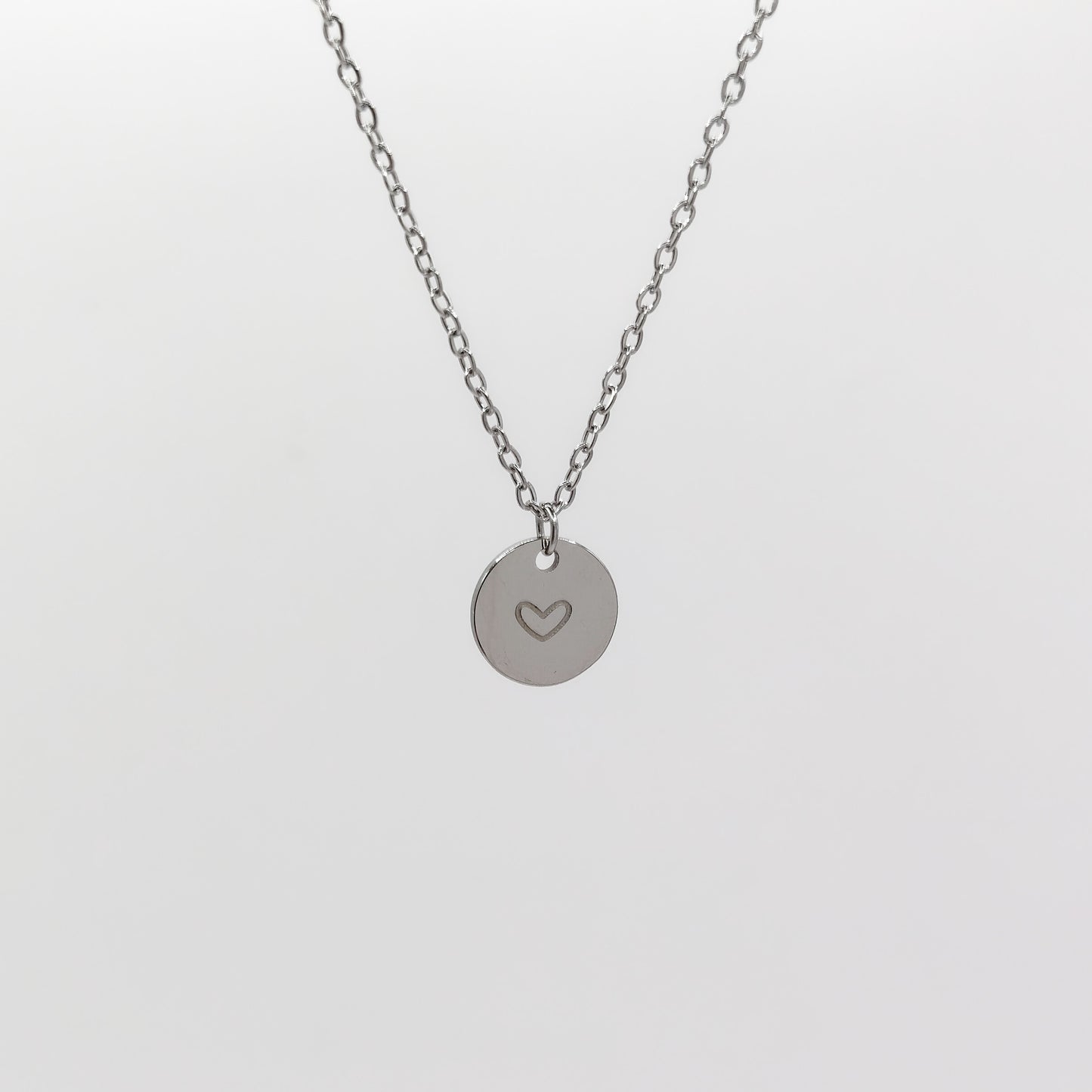 A close-up view of the stainless steel circular disc charm, showcasing the cleanly stamped heart outline and the delicate 1.5mm chain structure.