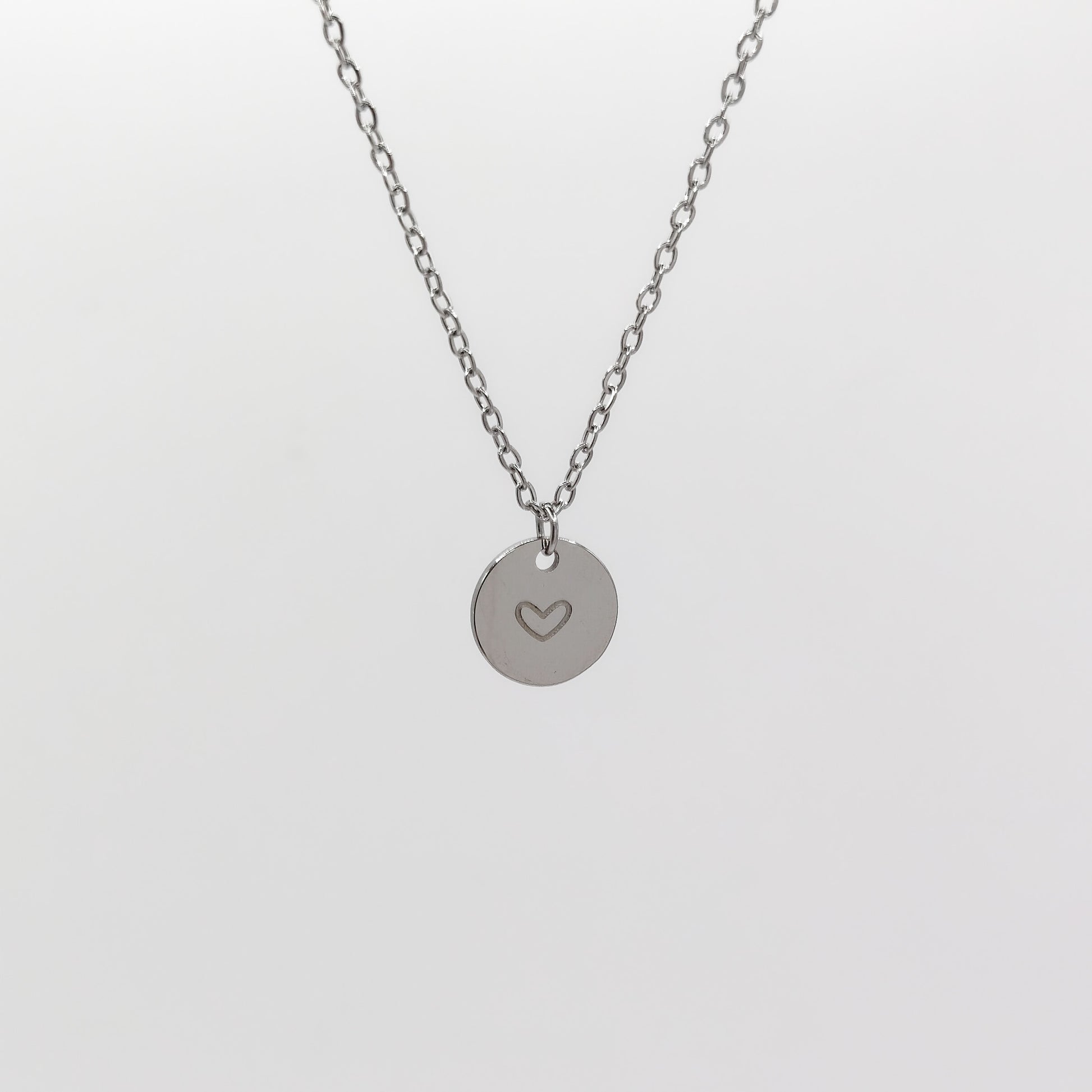 A close-up view of the stainless steel circular disc charm, showcasing the cleanly stamped heart outline and the delicate 1.5mm chain structure.