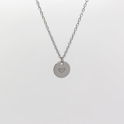 A close-up view of the stainless steel circular disc charm, showcasing the cleanly stamped heart outline and the delicate 1.5mm chain structure.