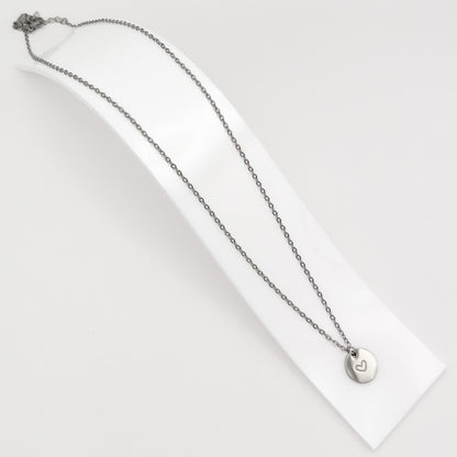 Silver plated stainless steel cable chain necklace featuring a minimalist round disc pendant with an engraved heart, displayed on a curved white stand.